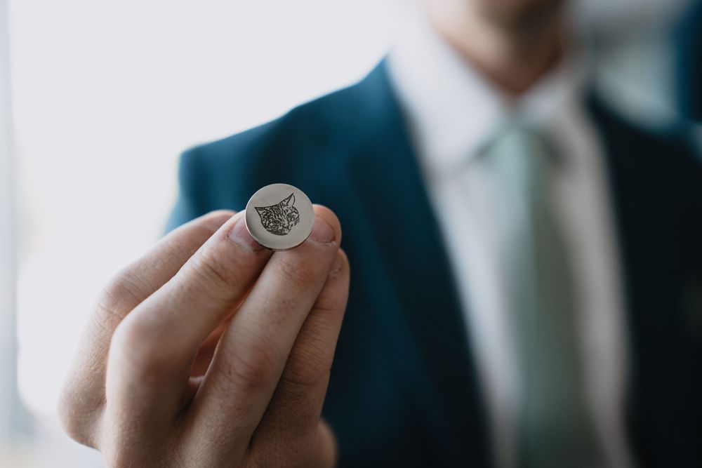 Man in blue suit holding a small round coin with a cat engraving between his fingers.