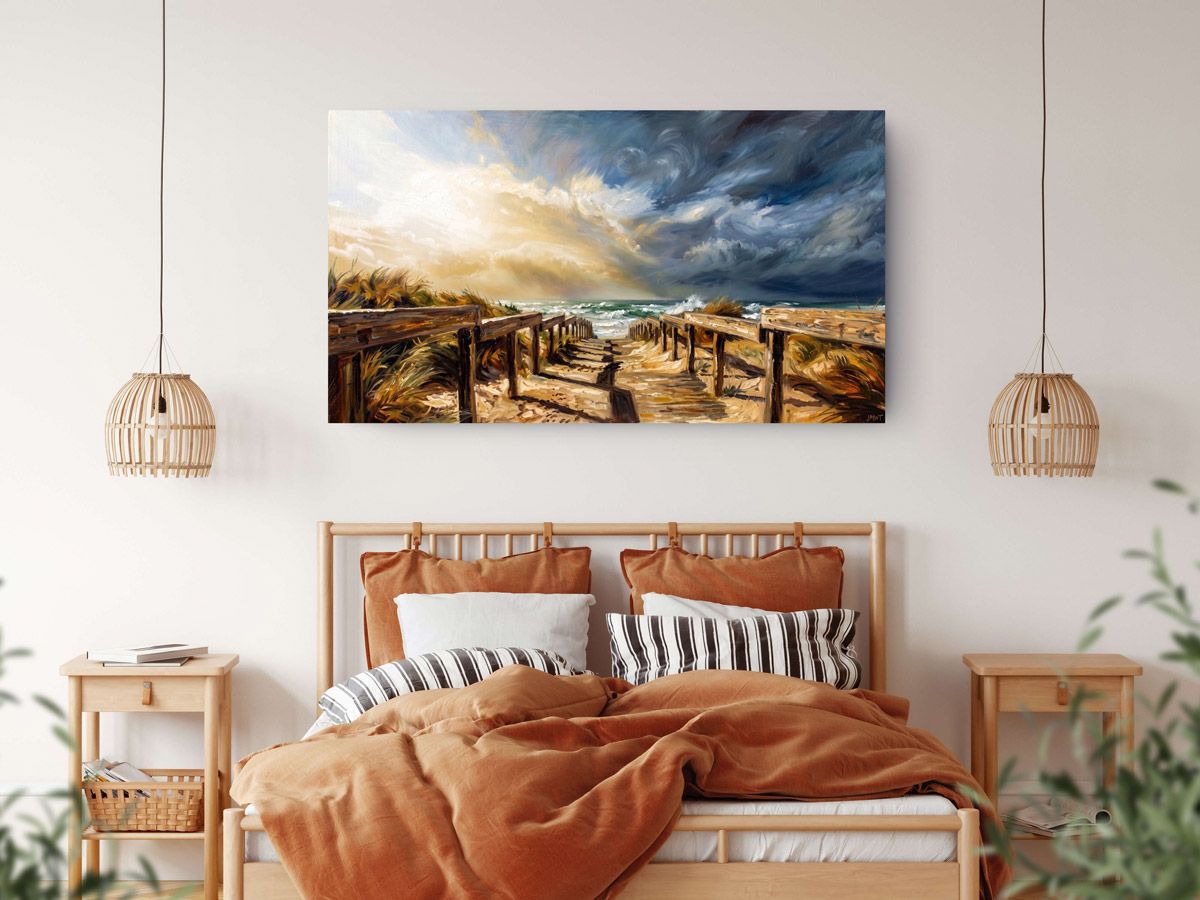 Dramatic stormy beach canvas wall art above a boho bedroom bed with warm terracotta bedding and rattan furniture.