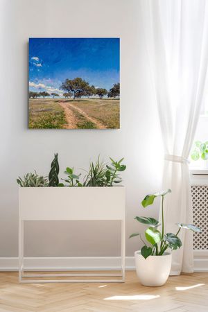 A canvas painting of a sunny dirt path through green fields with trees hangs above a white planter with houseplants.