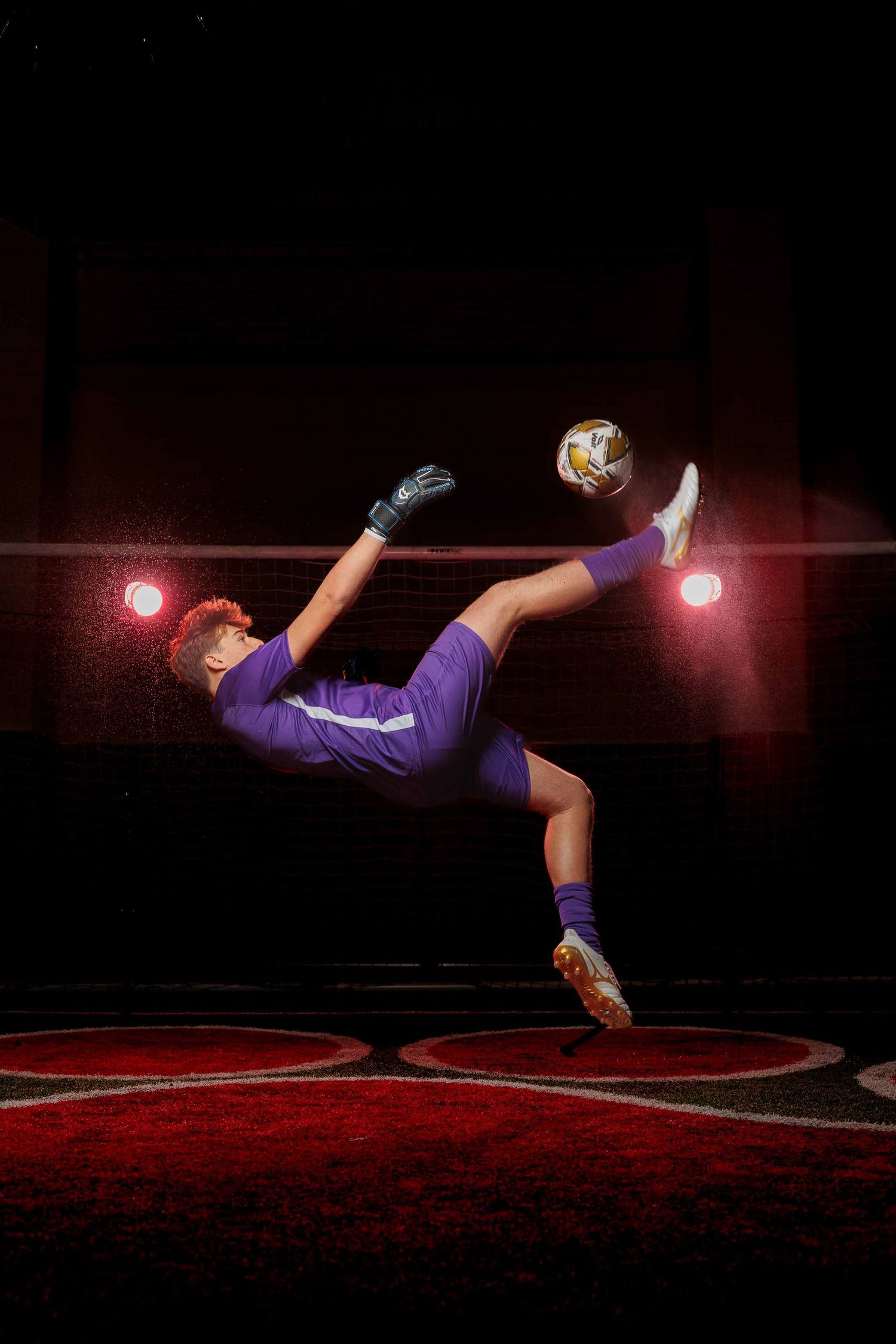 Soccer player in purple uniform performs a bicycle kick under dramatic stadium lights on a dark field.