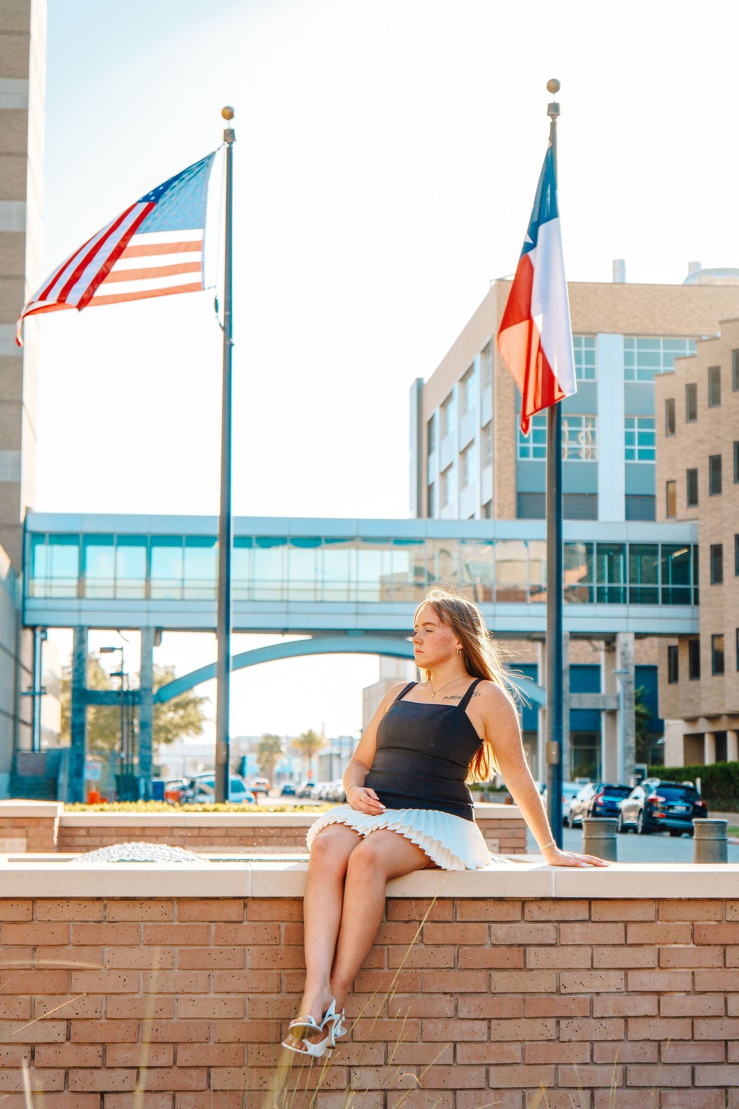 Young woman in light blue dress joyfully tossing graduation cap in front of a classic university building.