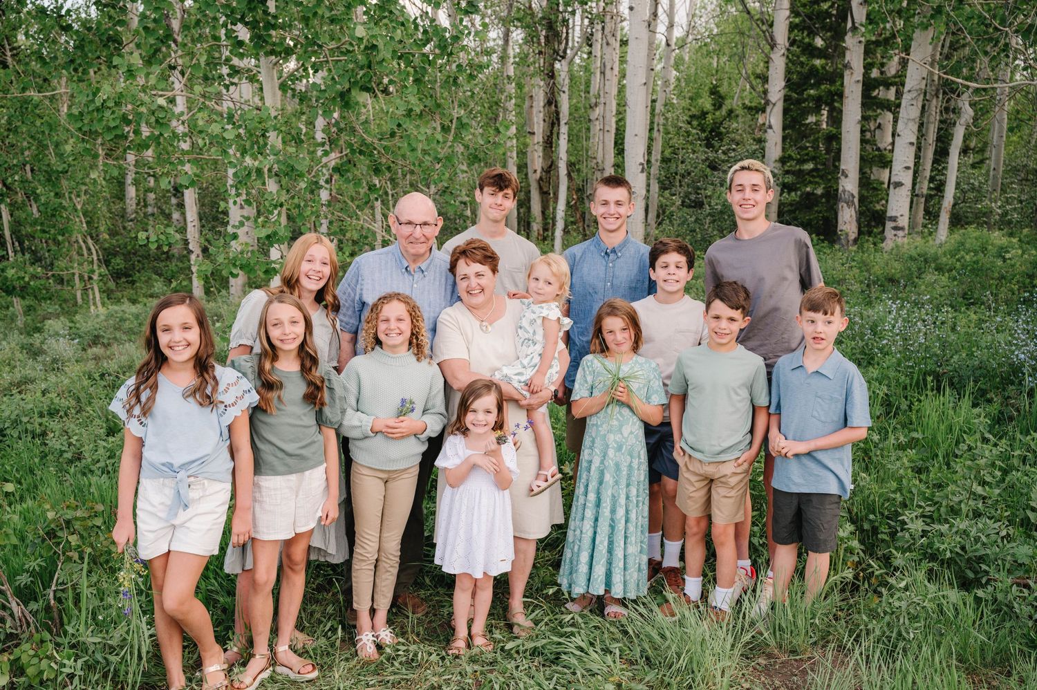 Family group portrait in coordinated blue and white outfits standing in a wooded forest setting.