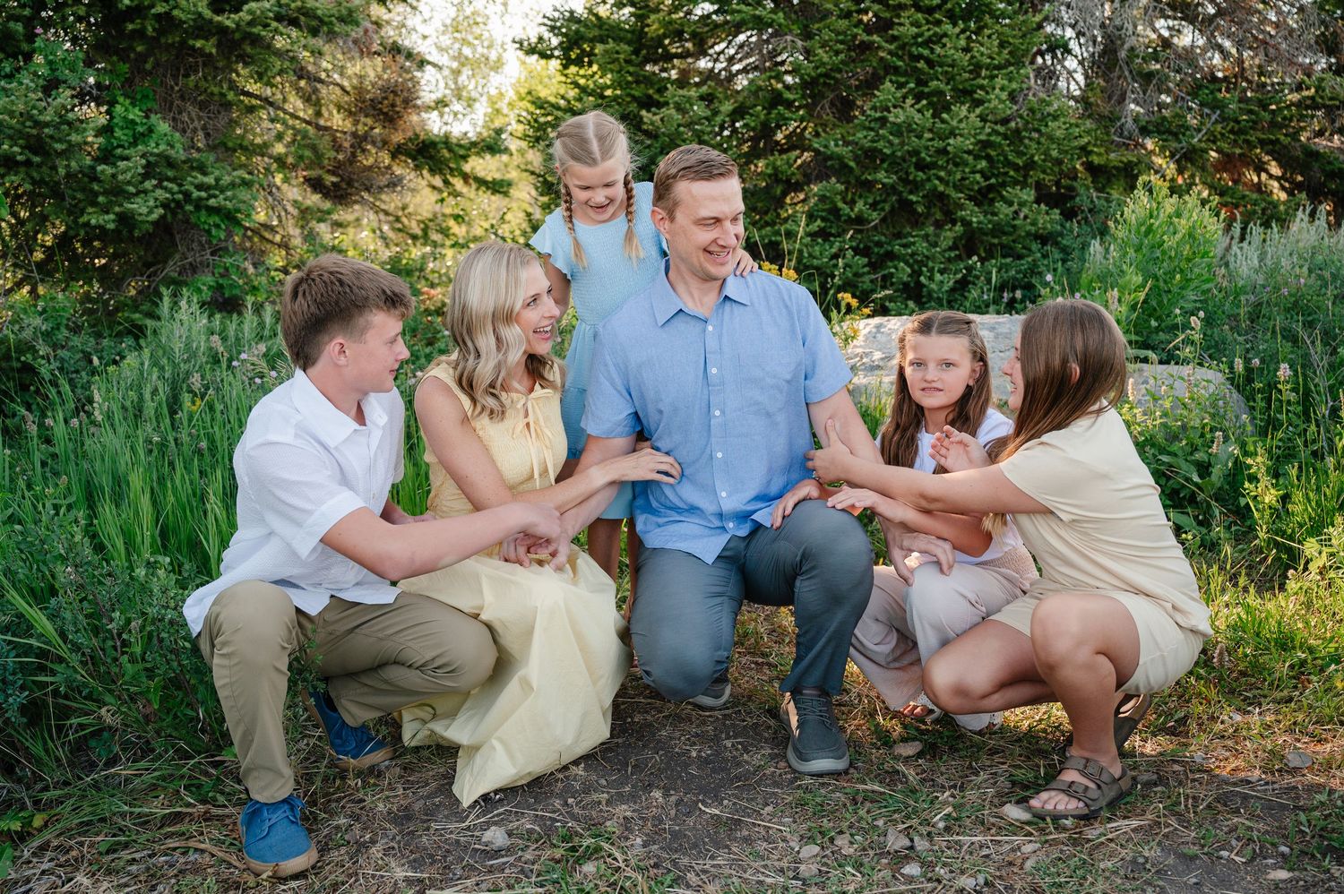 Happy family of six poses outdoors in a lush green garden setting during a professional portrait session.