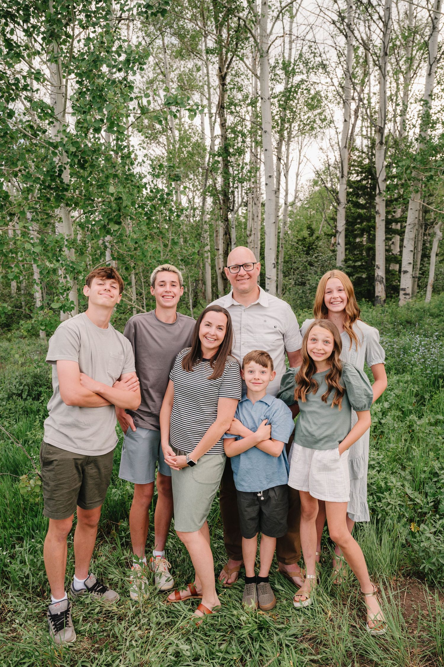 A group poses together in a scenic aspen grove with lush green foliage in the background.