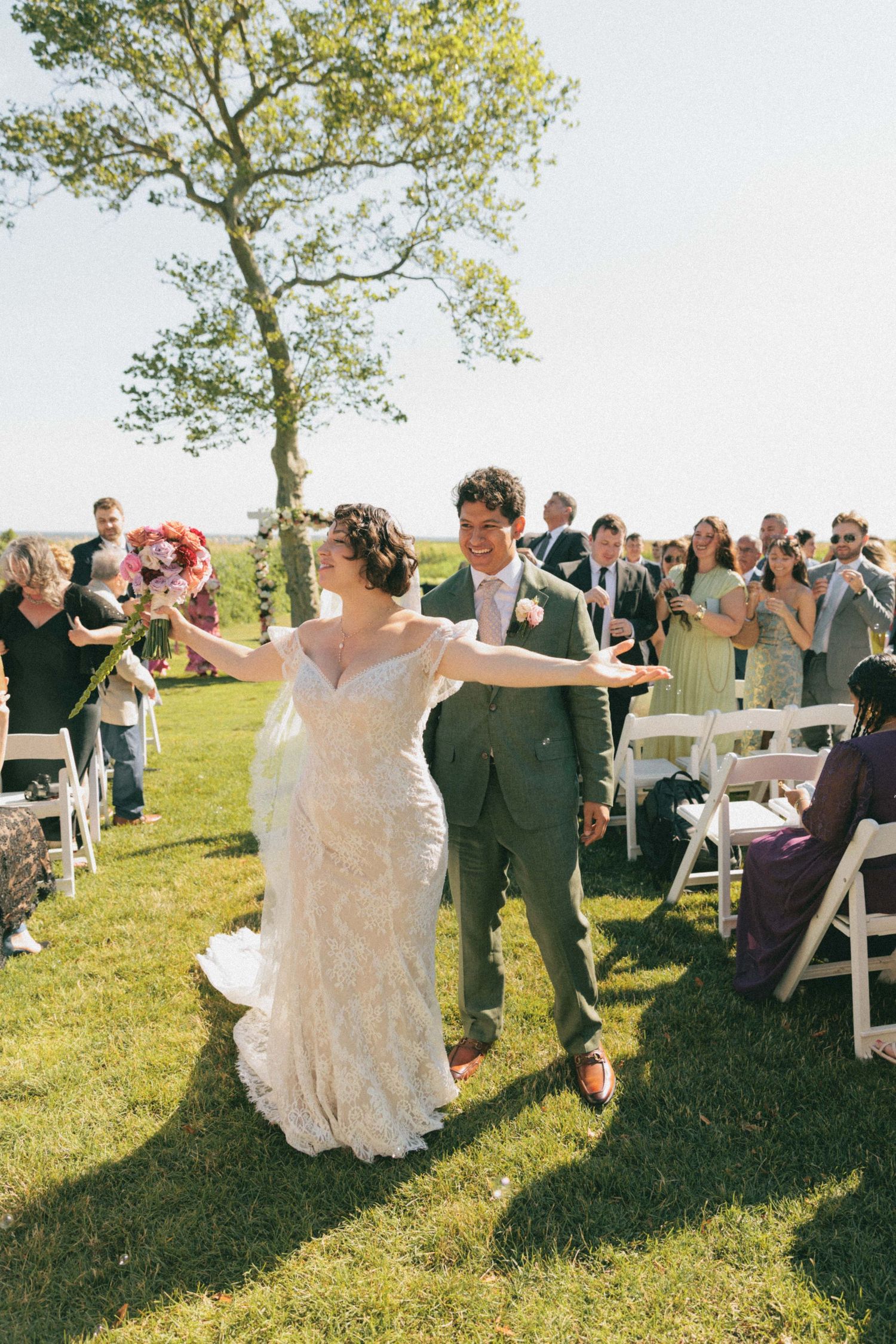 Joyful bride and groom walking down the aisle after outdoor wedding ceremony with guests cheering.