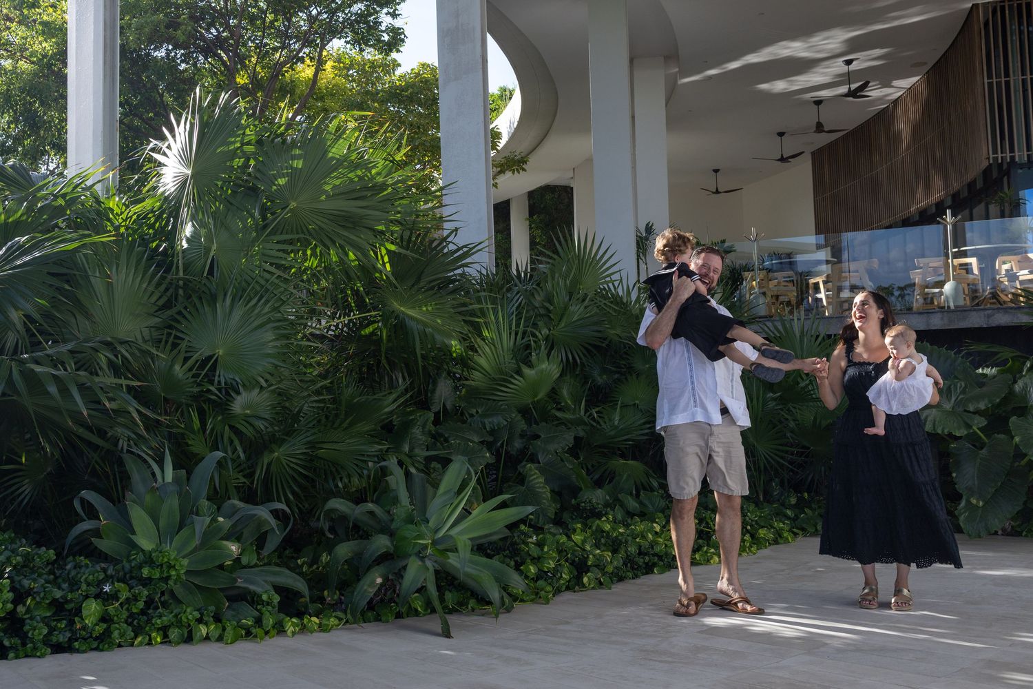 Family of four with two young children posing outdoors near lush tropical greenery at a luxury resort.