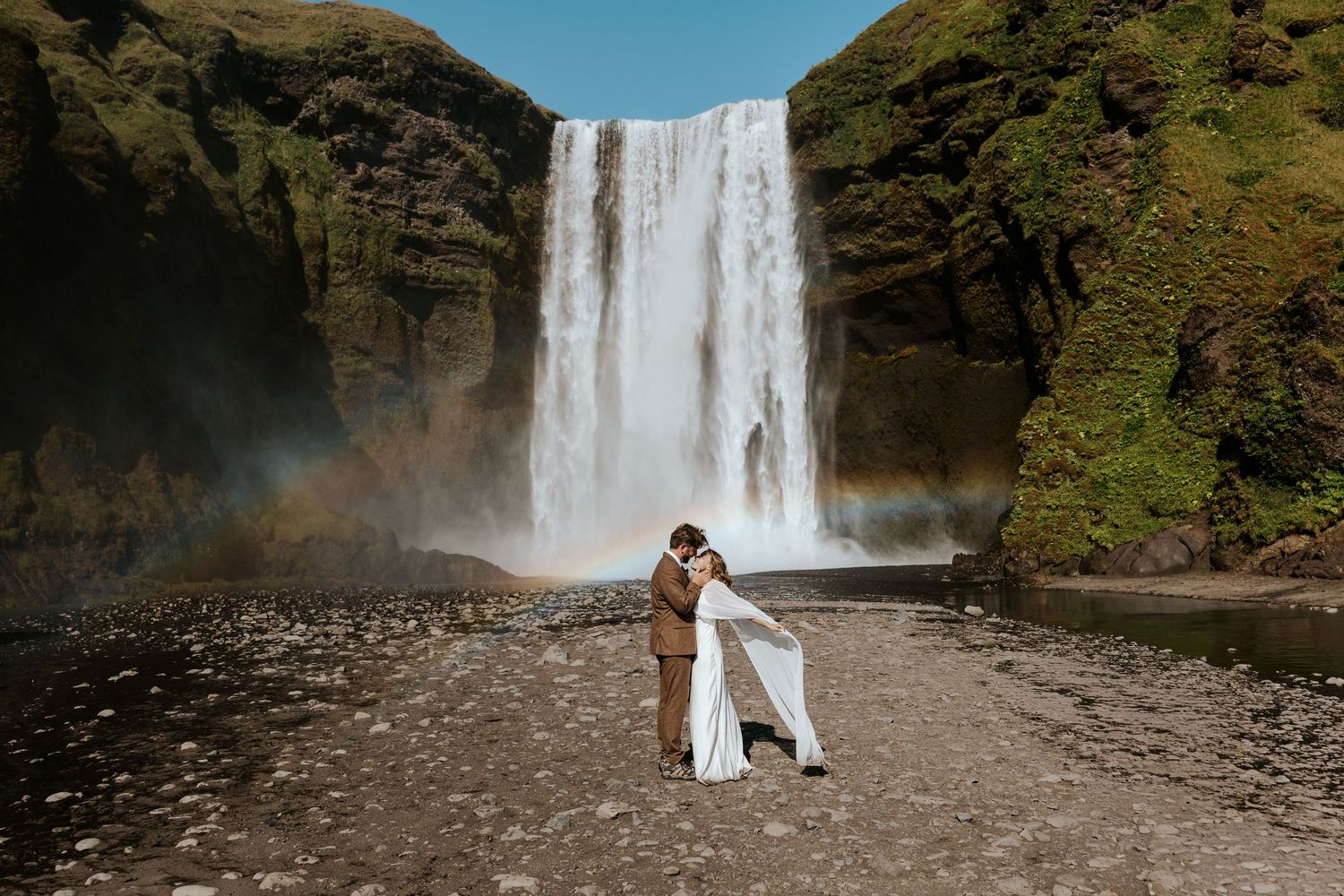 couple eloping at Skógafoss in Iceland moments away from kissing in front of the waterfall and rainbows