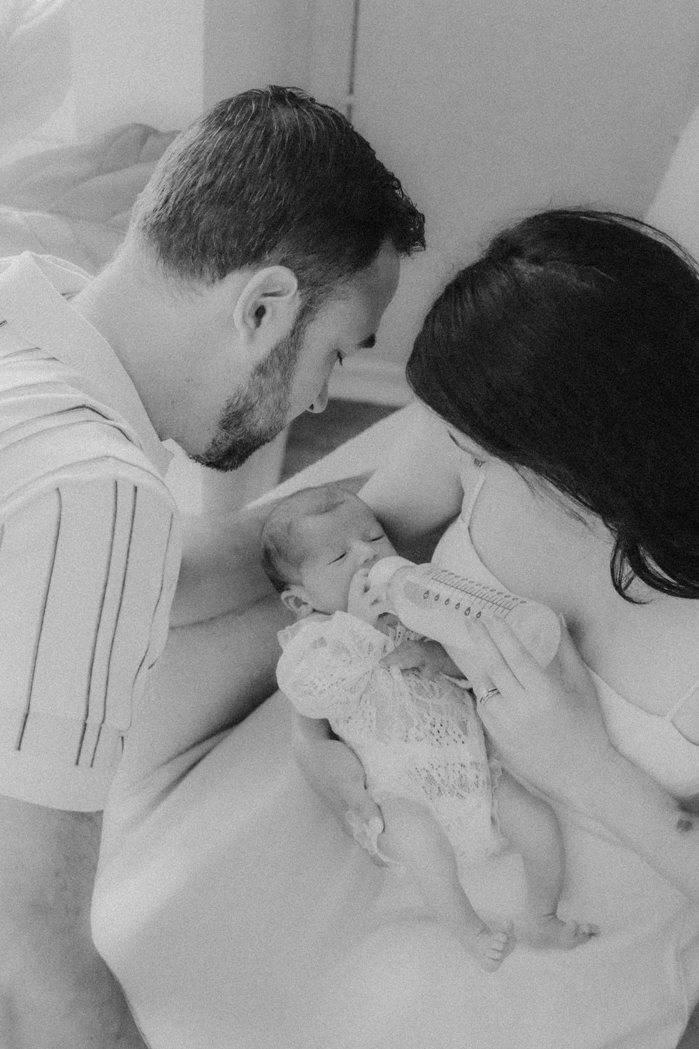 Black and white photo of new parents lovingly gazing at their newborn baby wrapped in a knit blanket.