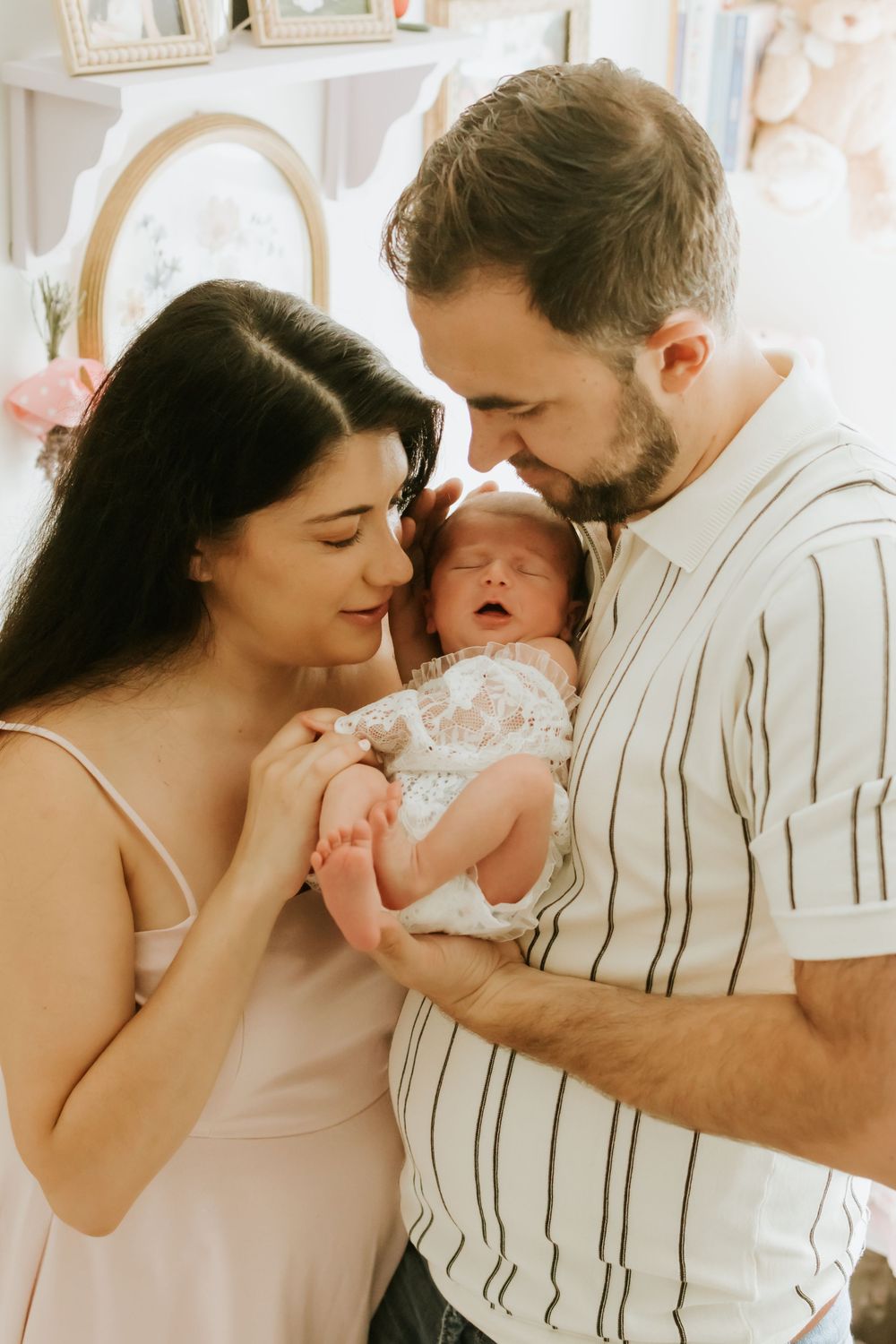New parents lovingly cradle their newborn baby in a softly decorated nursery room.