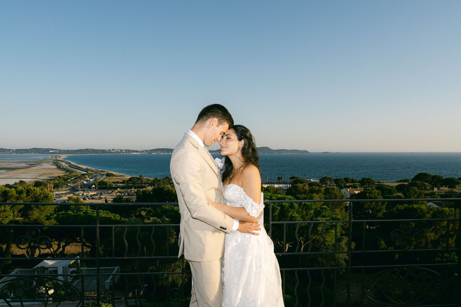 Couple embraces on a scenic overlook with ocean and coastline views during golden hour at their outdoor wedding.