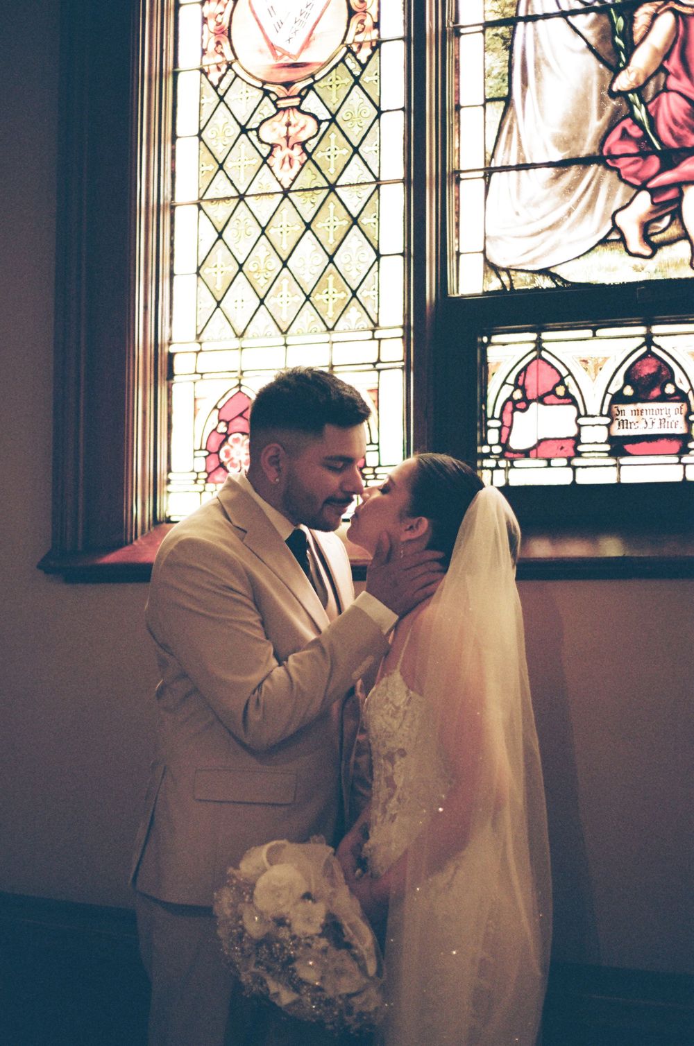 A bride and groom share a romantic moment in front of a stunning stained glass church window.