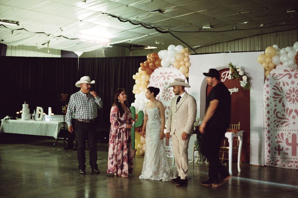 Wedding ceremony in decorated hall with balloon arch, bride and groom with guests in formal attire.