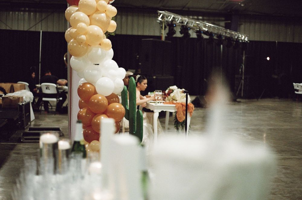 Balloon column arch in gold and white beside a decorated table in a large event hall with stage lighting.