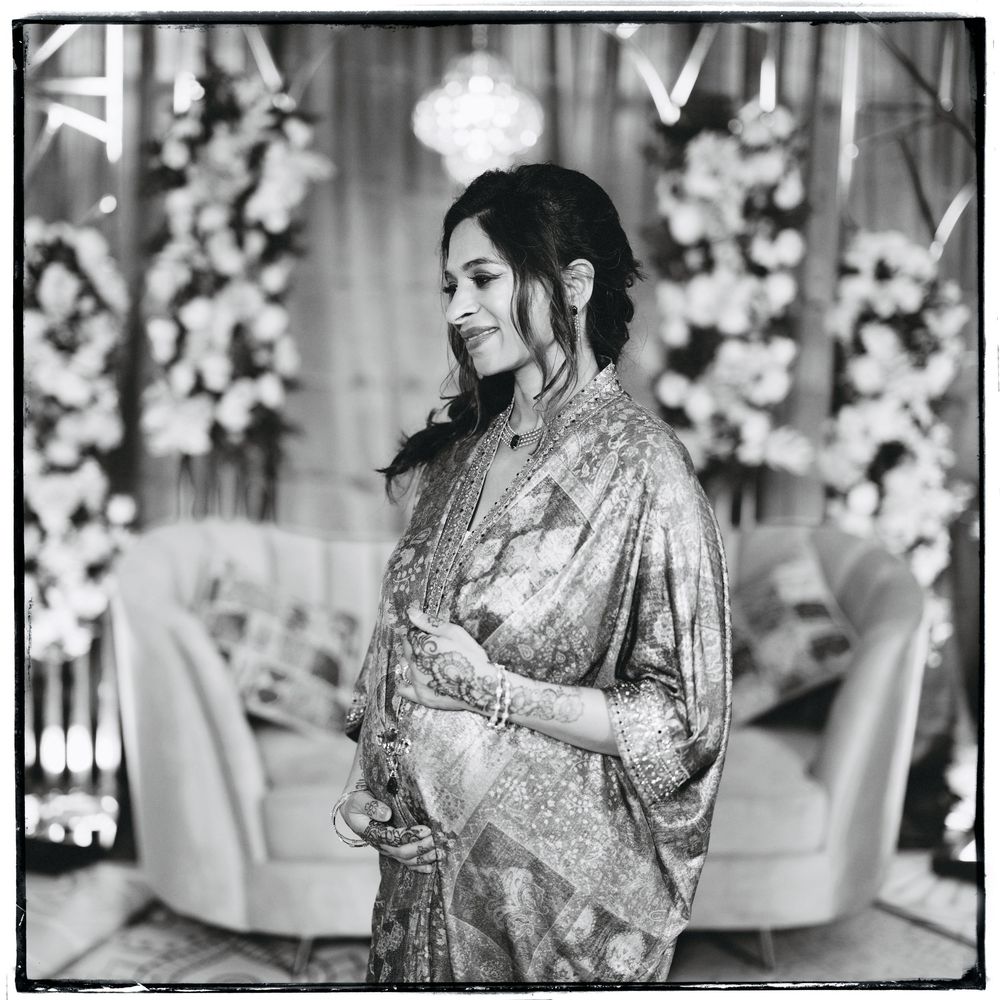 Elegant woman in embroidered saree with floral backdrop at Baby Shower ceremony, black and white photo.