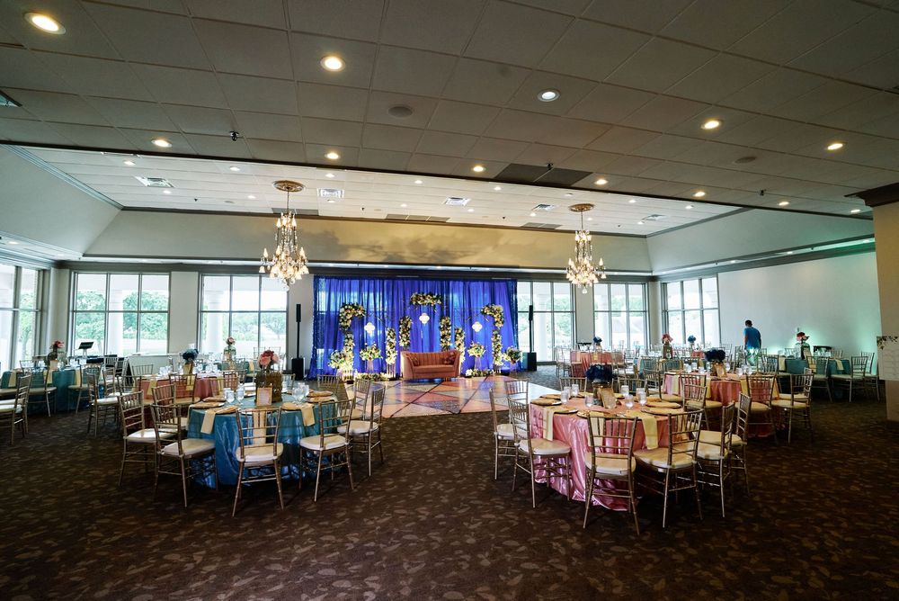 Elegant banquet hall with colorful table settings, chandelier lighting, and a decorated stage backdrop for a special event.