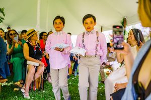 Two young ring bearers in pink shirts and suspenders walk down the aisle at an outdoor wedding ceremony.