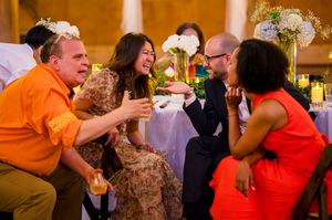Four guests laughing and toasting drinks together at a festive wedding reception dinner table.