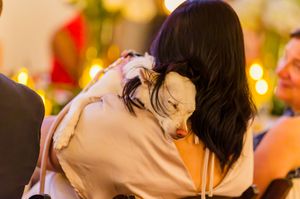 Woman with dark hair hugging a small white dog at a festive event with bokeh lights in the background.