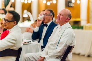 Men laughing and enjoying themselves at a formal wedding reception dinner in an elegant venue.