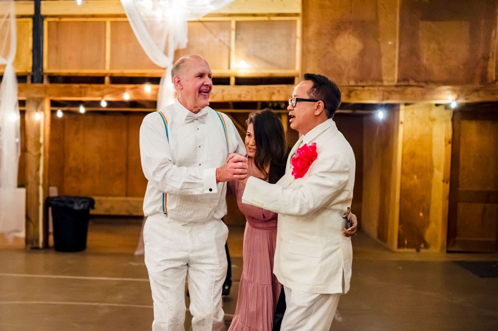 Three people laughing and celebrating together at a wedding reception in a rustic barn venue.