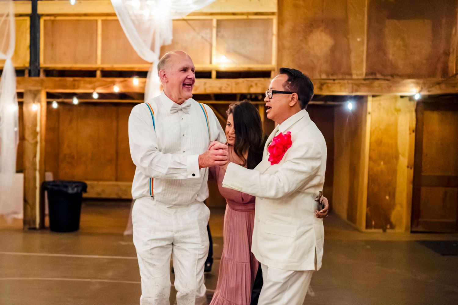 Three people laughing and celebrating together at a wedding reception in a rustic barn venue.