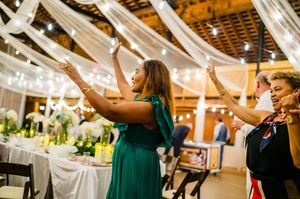 Two women dancing joyfully at an elegant wedding reception with string lights and white draping.