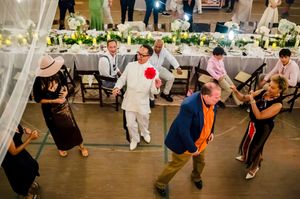 Guests dancing joyfully at an elegant wedding reception with floral centerpieces and long decorated tables in background.