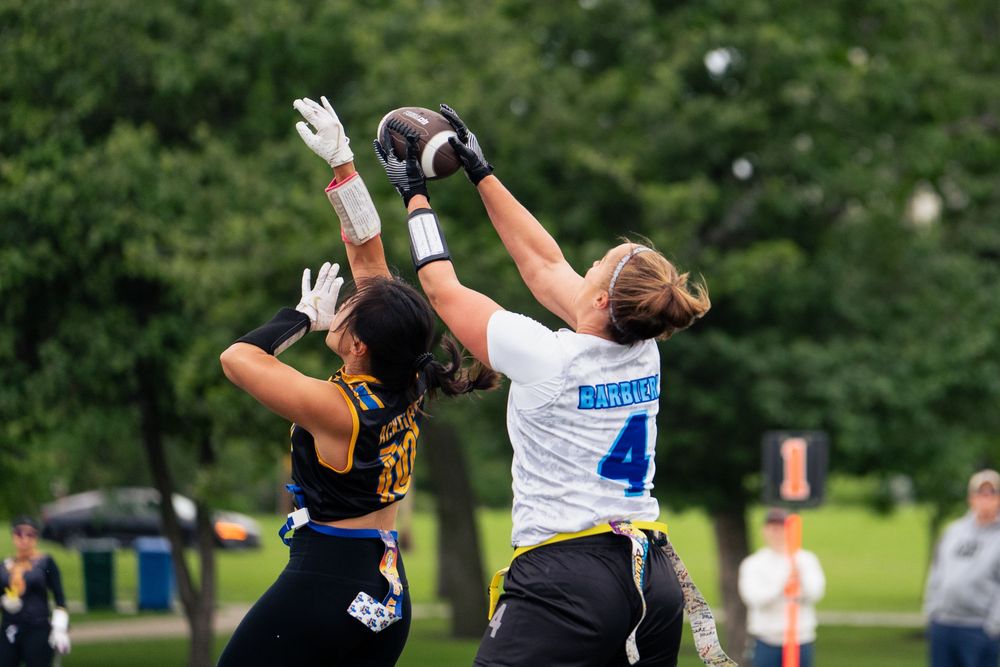 Two opposing flag football players vie for a football in the air at Pride Bowl hosted by NGFFL in Chicago