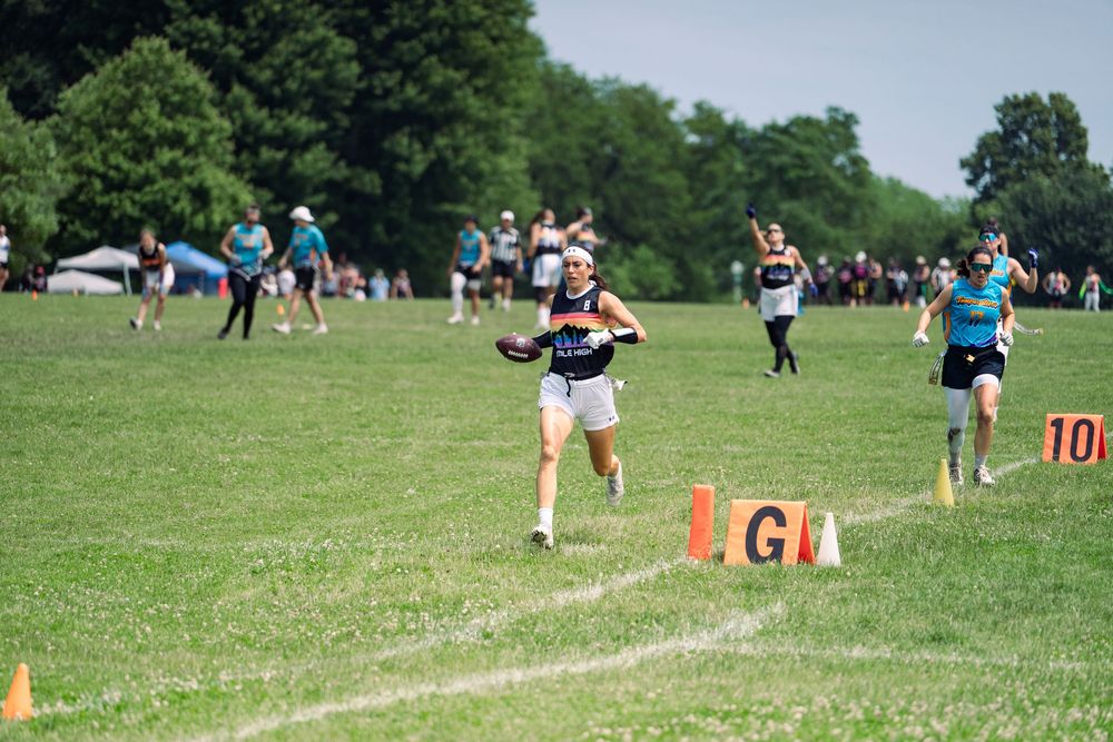 A flag football athlete runs downfield with the ball completing a touchdown with trailing defenders behind her at Pride Bowl hosted by NGFFL