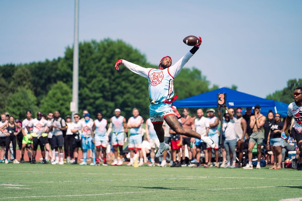 A football player from Chicago attempts to make a one-handed catch on the field with spectators looking on at Pride Bowl, hosted by NGFFL