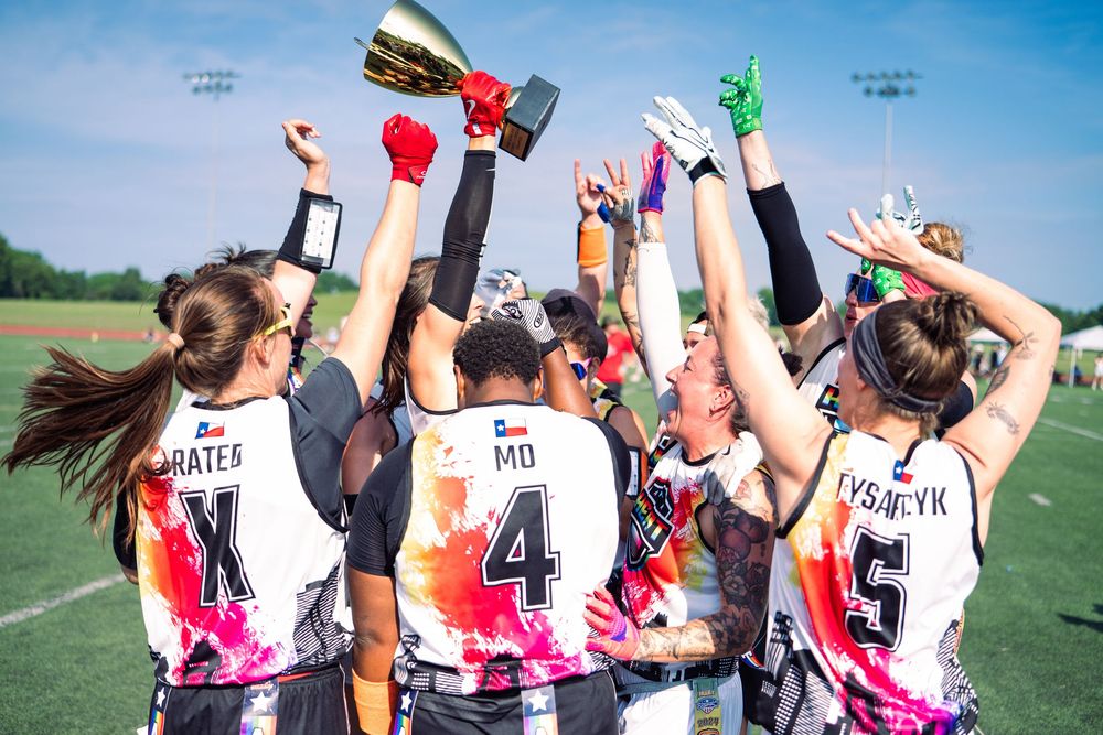 An Atlanta women's+ flag football team celebrates a championship at Pride Bowl hosted by NGFFL with a trophy hoisted in the air in Chicago