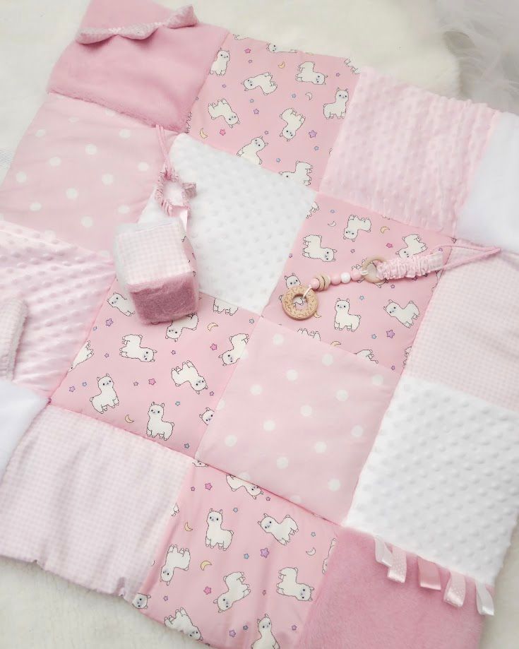 Pink patchwork baby blanket with unicorn print, polka dots, and white minky fabric squares, with small accessories.