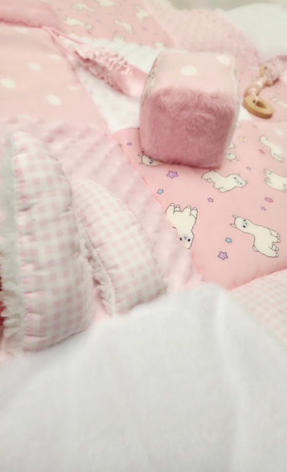 Pink baby blankets with gingham and polka dot patterns, a pink felt cube toy, and cute animal print fabric arranged softly.