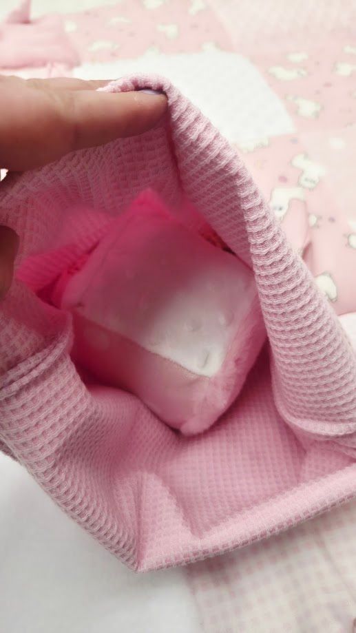 A hand holding a pink waffle-textured pouch containing a white soap bar, set against a pink floral background.