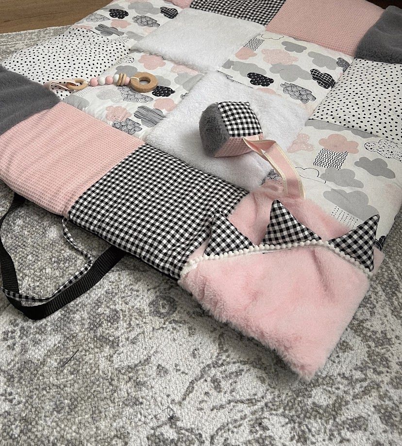 Pink, gray, and black patchwork baby play mat with matching accessories including a rattle and hat.