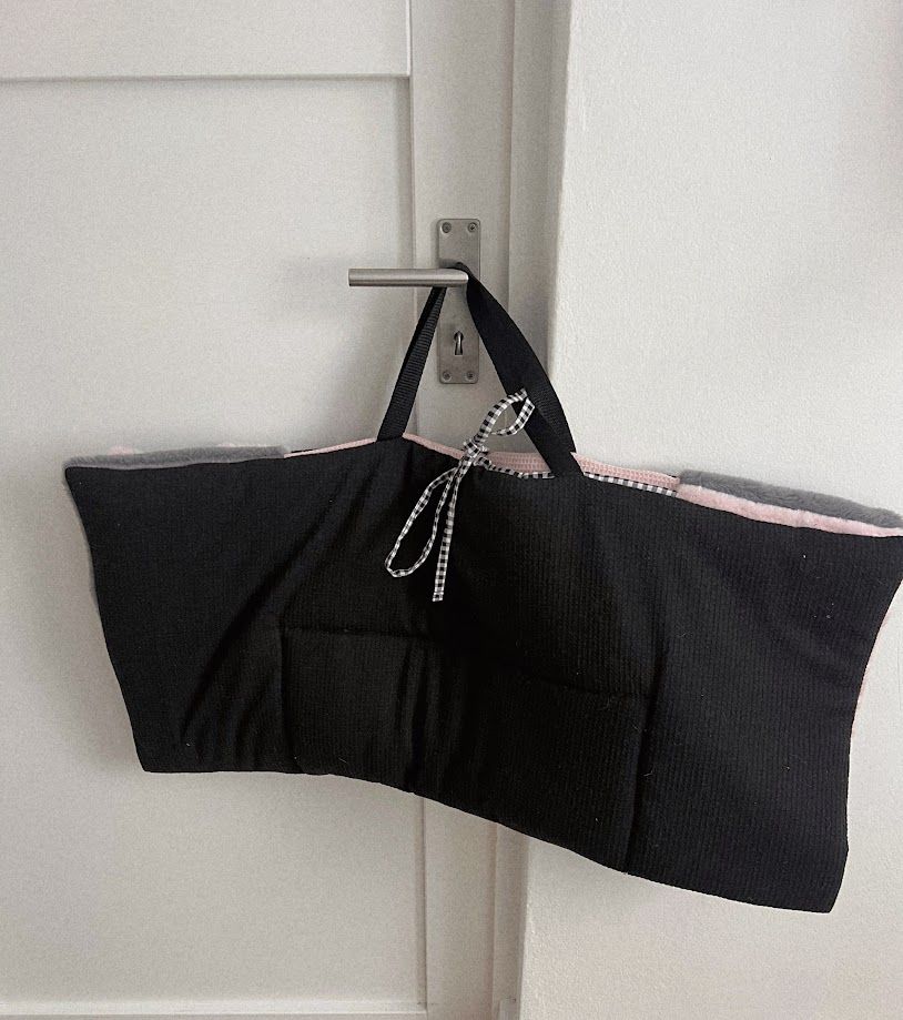 Black bandeau bra with pink trim and rhinestone bow detail, hanging on a door hook with tags attached.