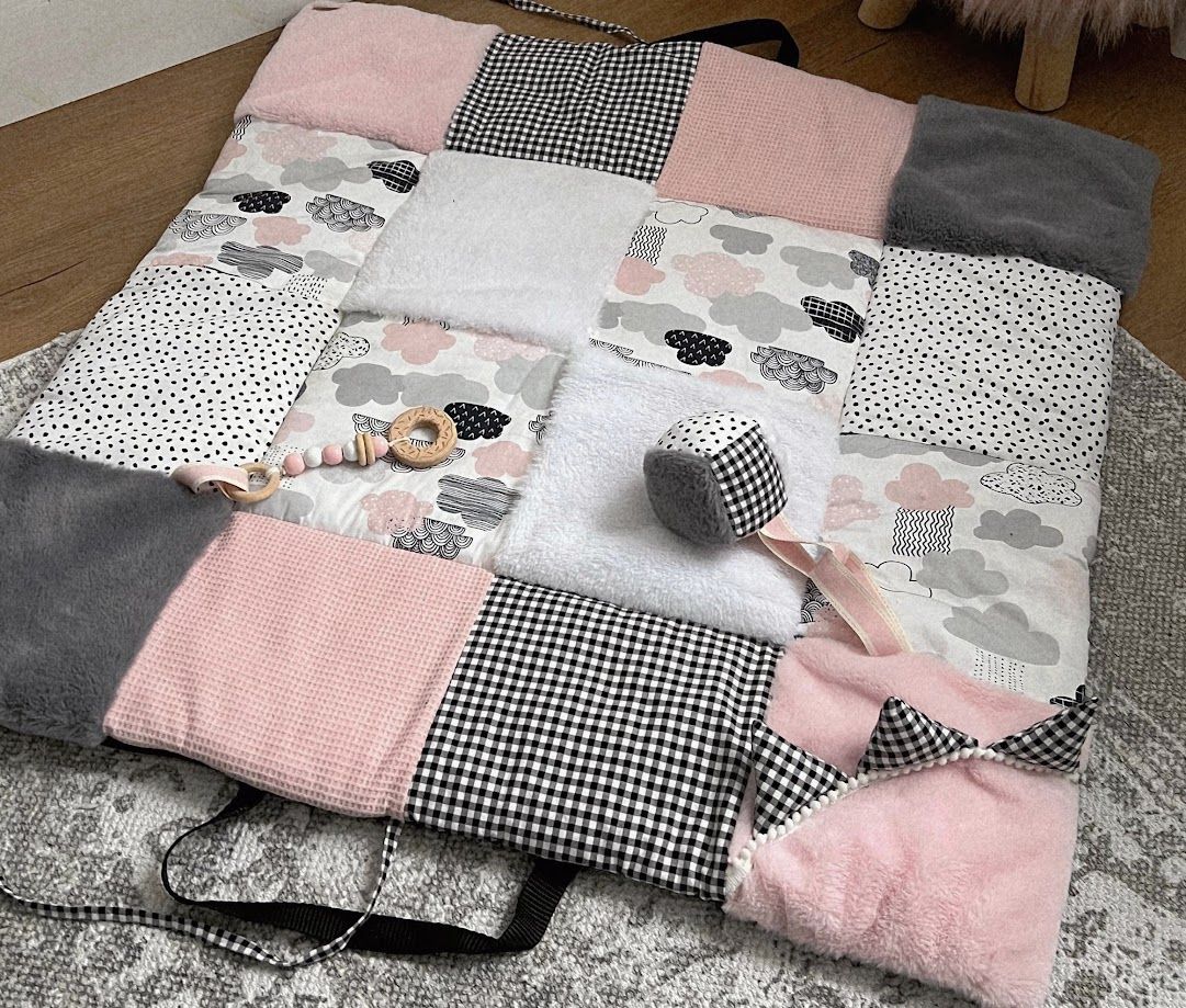 Handmade patchwork baby play mat in pink, grey, and black gingham with cloud motifs and wooden teething toys.