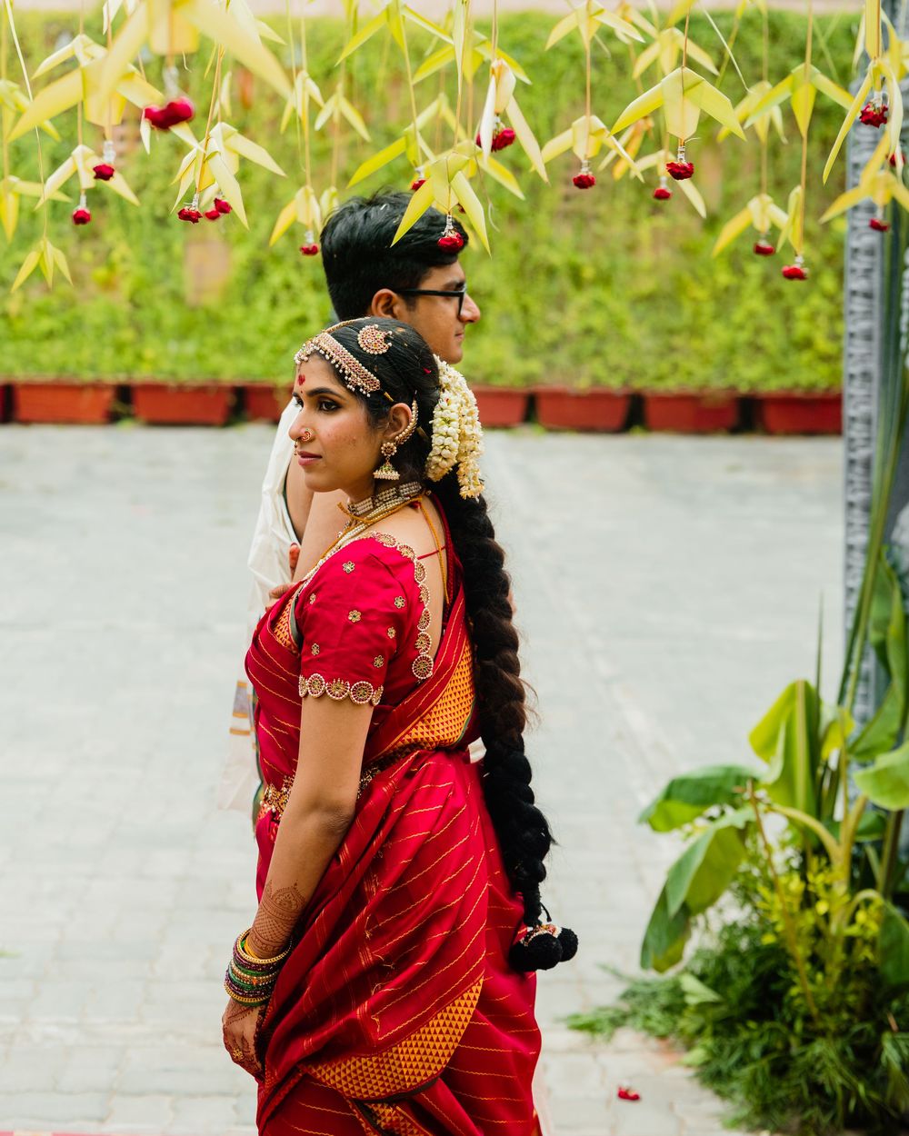 South Indian bride in red saree with groom during traditional wedding ceremony outdoors.