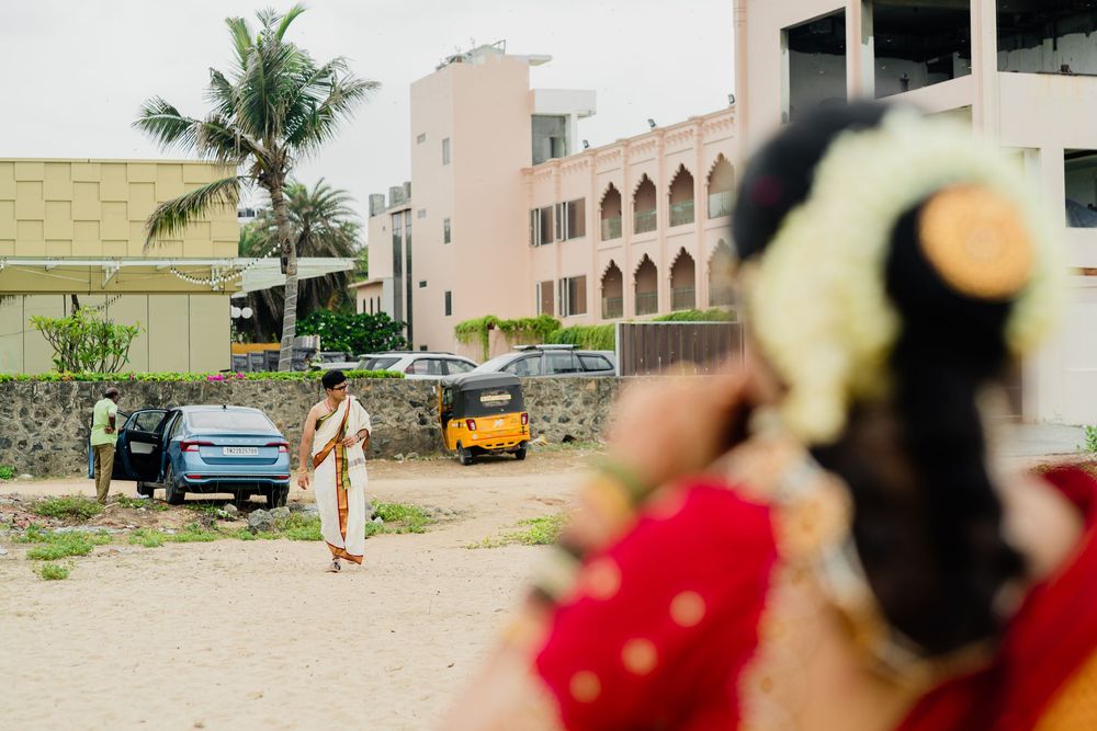 Indian bride in red saree with floral hair accessory at outdoor wedding venue with palm trees.