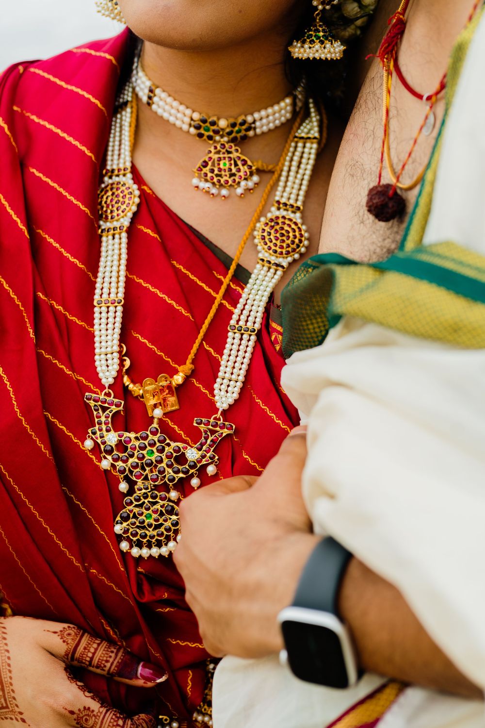 Indian bride in red saree wearing traditional gold and pearl bridal jewelry including elaborate necklace and earrings.