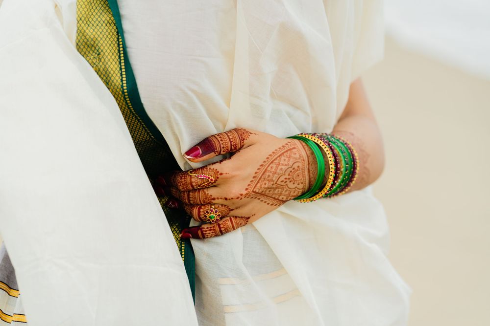 Close-up of a bride's hand adorned with intricate henna and green gold bangles, resting on a white saree.