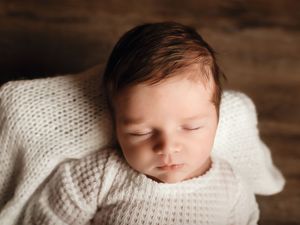 Peaceful newborn baby sleeping wrapped in a soft white knit blanket, with dark hair and delicate features.