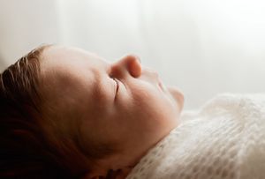 Peaceful newborn baby sleeping wrapped in a soft white blanket in a serene, softly lit setting.