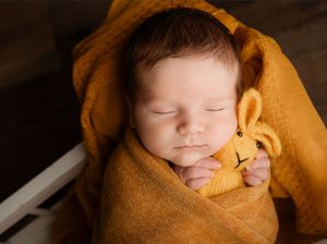 Sleeping newborn baby wrapped in a cozy mustard yellow blanket, holding a matching knitted bunny toy.