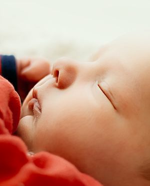 A peaceful newborn baby sleeping soundly, dressed in red, with soft delicate features and closed eyes.