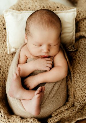 Peaceful newborn baby sleeping wrapped in a soft beige blanket on a knit texture with a tiny pillow.