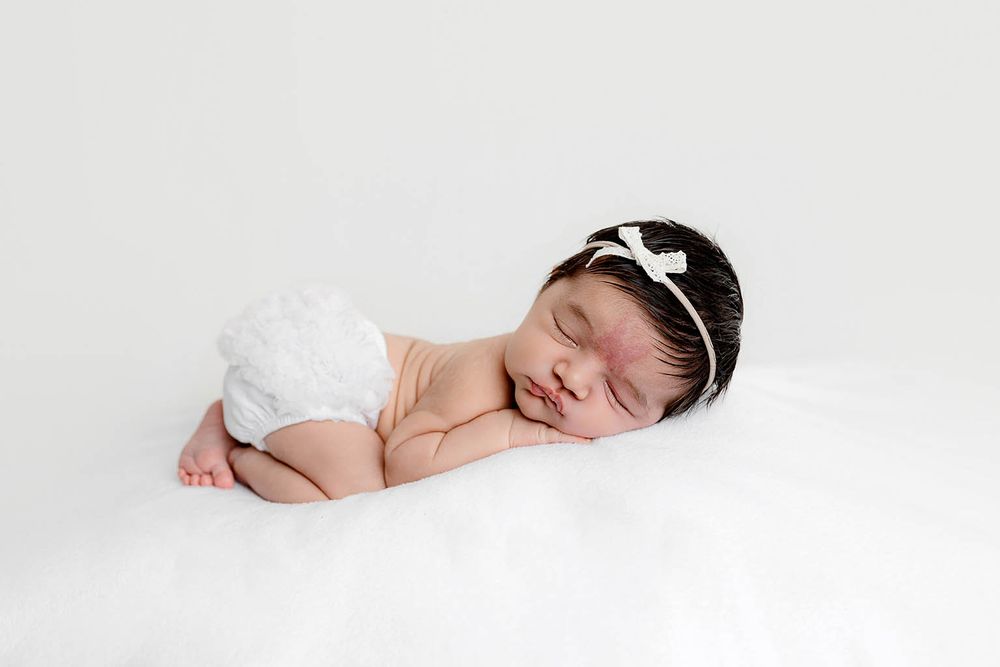 Sleeping newborn baby girl in white lace bloomers and bow headband on white background.