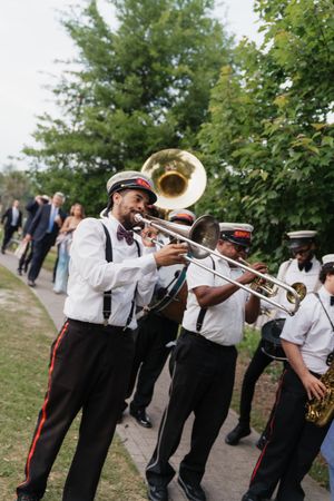 New Orleans brass band in uniform plays trombone leading a wedding second line parade outdoors.