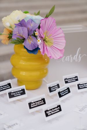 Yellow vase with purple and pink flowers beside black and white wedding escort cards.