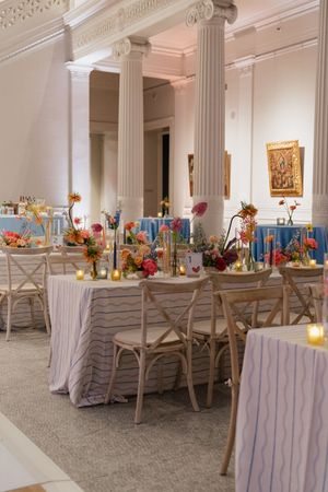 Elegant wedding reception hall with white columns, striped linens, cross-back chairs, and colorful floral centerpieces.